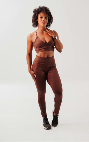 Woman wearing a IREP Stealth Wealth brown sports bra and leggings set on a white background